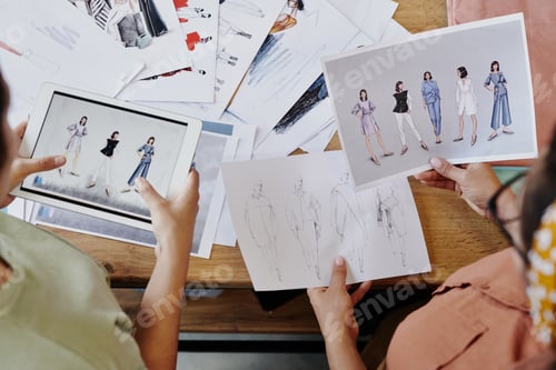 Preview: Hands of two fashion designers discussing their sketches of trendy clothes