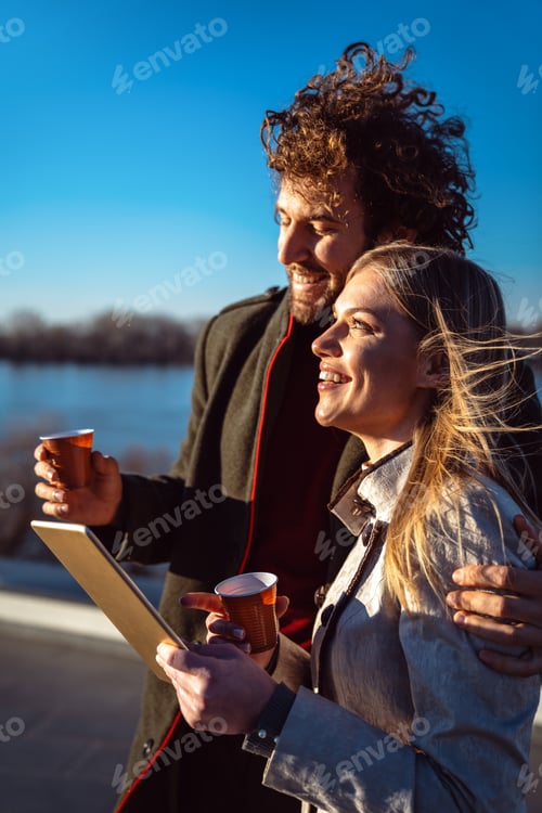 Preview: Happy couple outdoors using tablet together, enjoying sunny day, love, connection, digital lifestyle