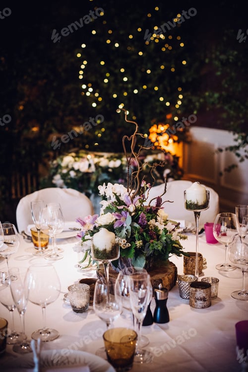 Preview: A table laid for a special occasion, with a floral centrepiece and candles, at night.