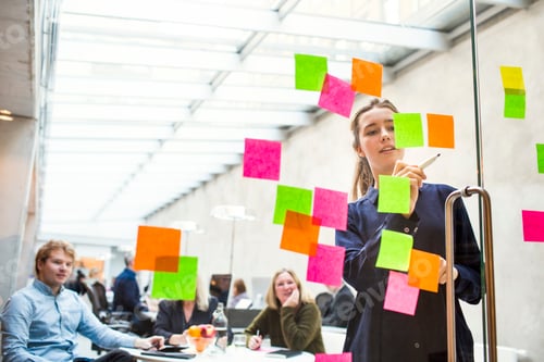 Preview: Young businesswoman giving presentation on sticky notes to colleagues in office