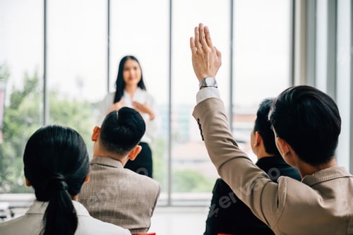 Preview: Active engagement is evident as a large group in a seminar classroom raises their hands to