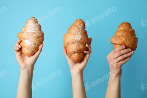 Preview: Hands holding croissants on blue background, close up