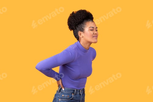 Preview: Young woman with back pain against a yellow background