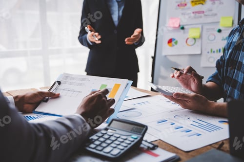 Preview: Young colleagues discuss business and analytical price charts using calculators and laptops to calcu