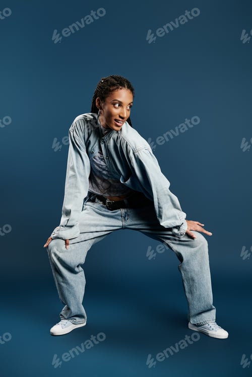 Preview: A fashionable young woman striking a playful pose in stylish denim against a striking backdrop