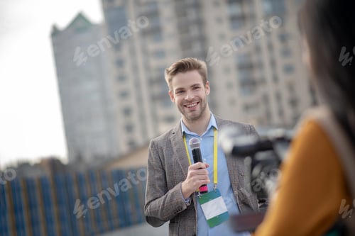 Preview: Young bearded reporter holding a microphone in his hand
