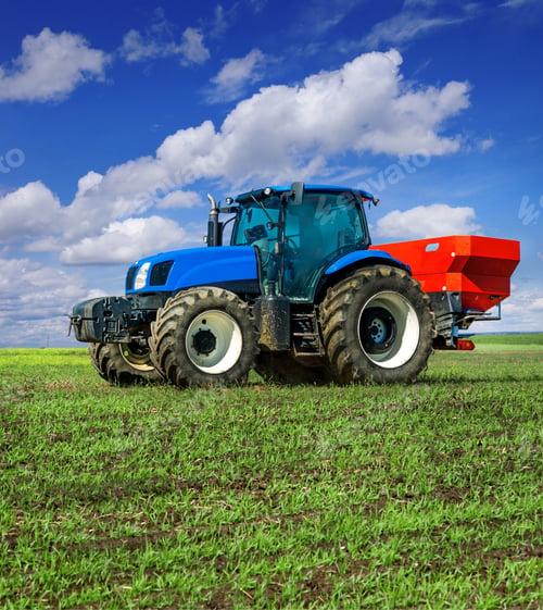 Preview: blue tractor in field work with modern red two-disc fertiliser spreader sprayer.