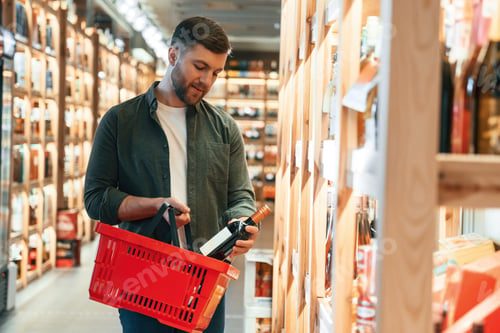 Preview: With shopping basket. Man is choosing wine in the store