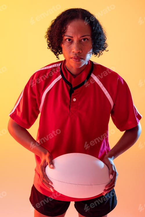 Preview: Portrait of african american female rugby player with rugby ball over neon yellow lighting