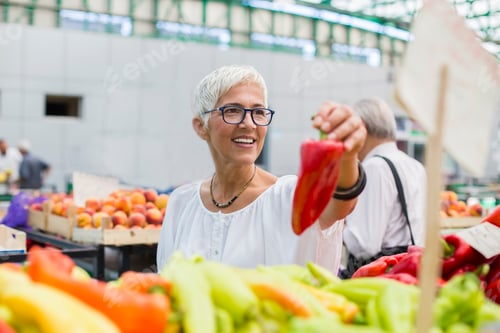 Preview: Good-looking senior woman wearing glasses buys pepper on market