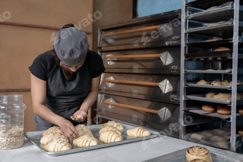 Preview: A young Hispanic baker is covering croissants with almond toppings before baking