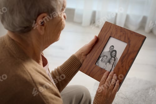 Preview: Elderly woman with framed family portrait at home