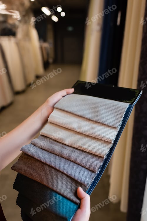 Preview: Cropped view of young woman holding cloth samples in blurred textile shop
