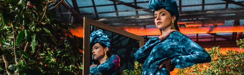 Preview: Panoramic shot of sensual woman in blue turban and dress standing near mirror in orangery