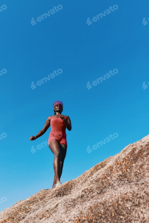 Preview: Woman in a red swimsuit walking on a rocky ledge under a clear blue sky