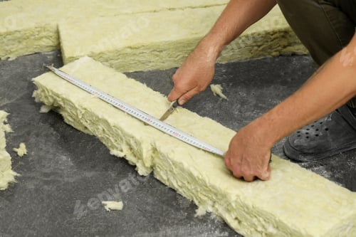 Preview: Worker measuring and cutting insulation material indoors, closeup