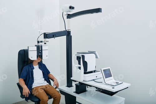 Preview: Boy has eye test in ophthalmological clinic looking through phoropter to eyes test chart. Eye test,