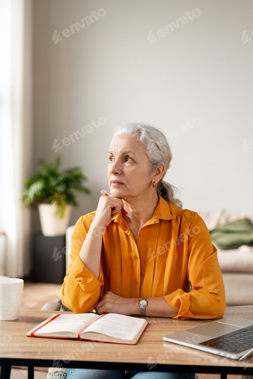 Preview: Senior woman contemplating new ideas with pen and notebook at home desk