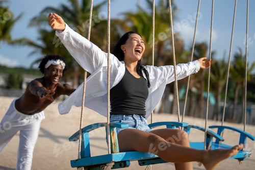 Preview: Happy interracial couple enjoying a fun beach day, swinging under palm trees on a tropical vacation
