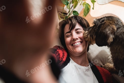 Preview: Young woman taking a selfie with mobile fun having fun with her pet dog indoors at home