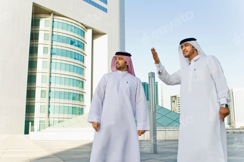 Preview: Two men in traditional attire engaging in conversation with modern cityscape in the background.