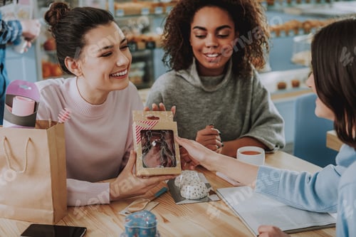 Preview: Cheerful Young Woman Sitting With Her Friends While Showing Baking Equipment