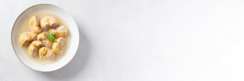 Preview: Traditional Catalan Christmas dish Escudella in white plate on table, stuffed pasta in meat broth, t