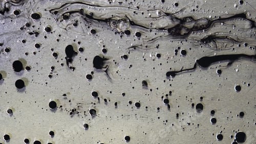 Preview: Top view of black ink drops flowing in liquid oil on metallic, grey background. Black balls of paint