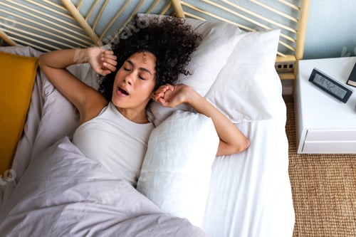 Preview: African American woman waking up in the morning, yawning and stretching arms in bed. Good morning.