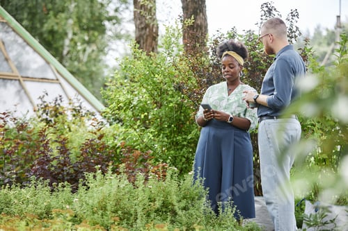 Preview: Black Female Landscape Architect Using Phone Talking to Male Client in Plant Nursery