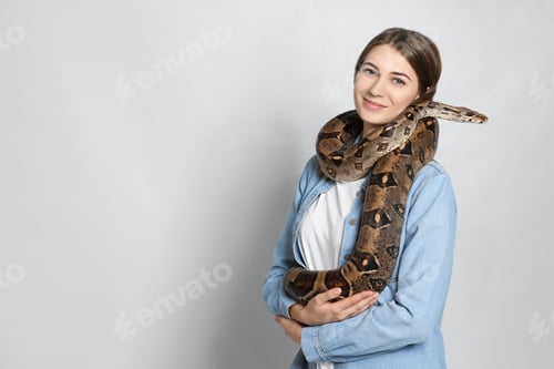 Preview: Young woman with boa constrictor on light background, space for text. Exotic pet