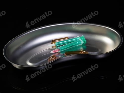 Preview: two syringes and broken ampules in a kidney basin on dark backgr