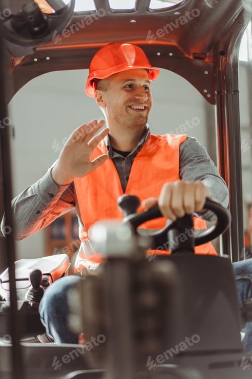 Preview: Handsome, smiling man, foreman sitting on forklift, waving his hand, looking away, greeting