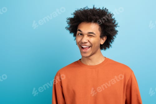 Preview: Young man smiling and winking against a blue background in a cheerful pose