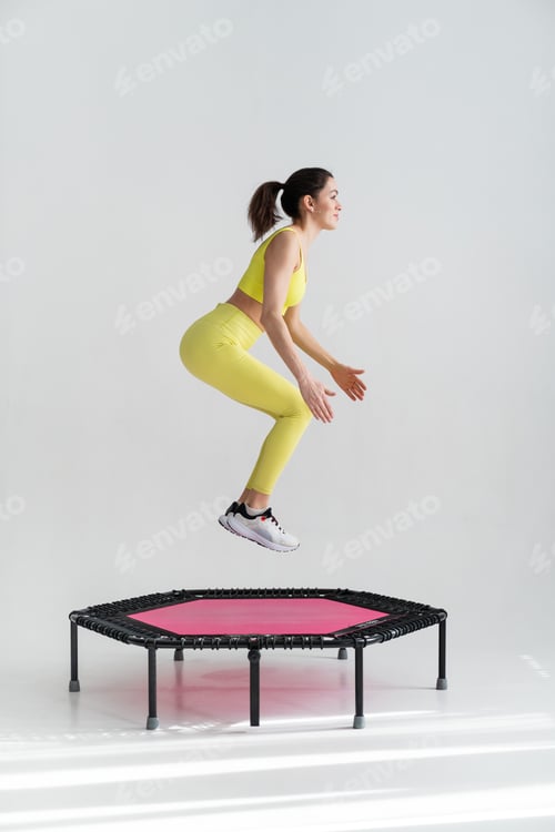 Preview: young fitness woman In sportswear jumping on sport trampoline White background