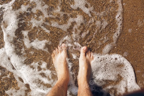 Preview: Top view of person feet in water on sandy beach and waves