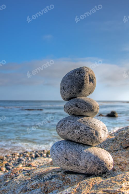 Preview: Selective focus shot of piled stones in a seashore with a blurred blue sky in the background