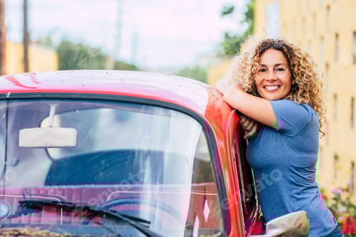 Preview: Portrait of happy middle age beautiful woman standing outside her red classic car and smiling