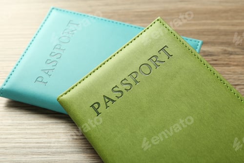 Preview: Two passports in bright covers on wooden table, closeup