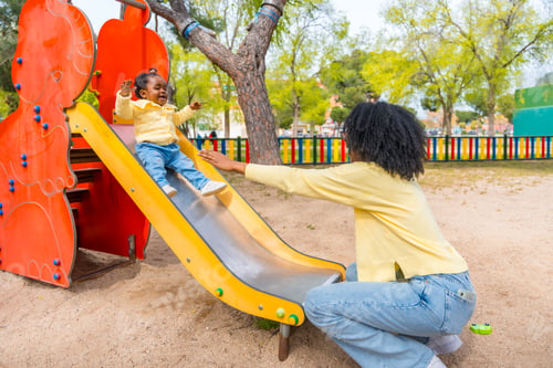Preview: Mother waiting beneath a slide for her african daughter