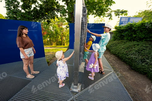 Preview: Mother with kids play with moving metal sticks frame at exhibition outdoor.