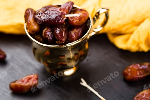 Preview: Dry fruit dates in golden cup near slate black heart. Copy space.