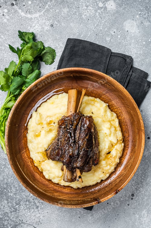 Preview: Braised lamb shank on the mashed potato in a plate. Gray background. Top view
