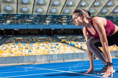Preview: athletic female runner in start position on running track at sports stadium