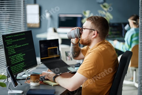 Preview: Young Adult Man Drinking Coffee While Working on Computer Coding