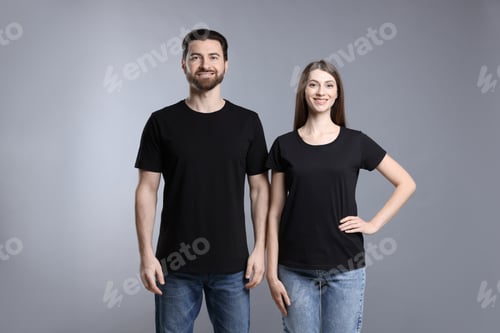 Preview: Woman and man wearing blank black t-shirts on light grey background. Mockup for design