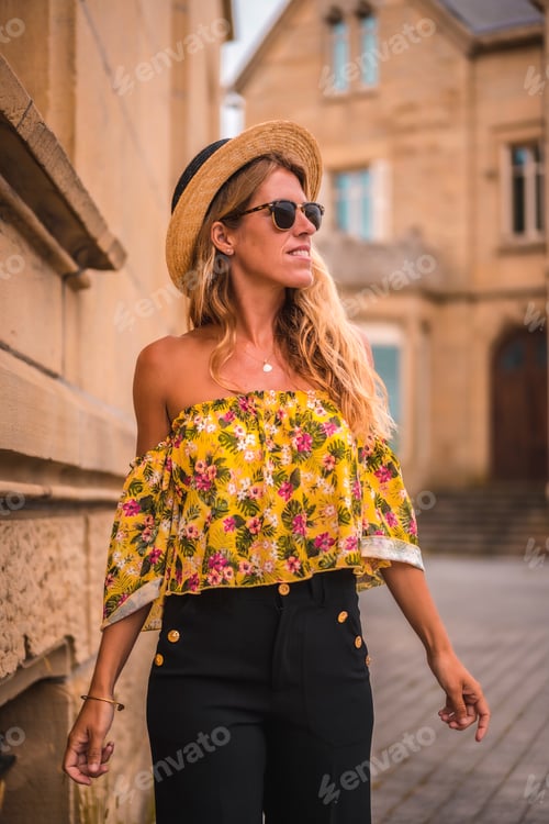 Preview: Blonde woman smiling with a yellow vintage outfit with a hat visiting a castle