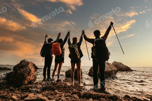 Preview: Group of hiker raised arms by the sea at sunset. View from behind.Teamwork and Adventure,travel.
