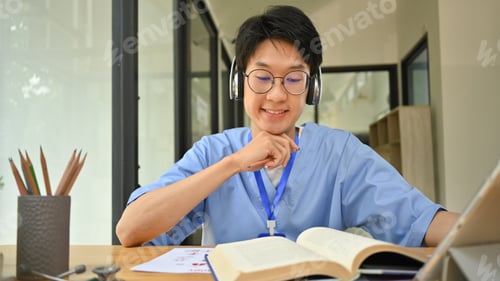 Preview: Asian male medical student in headphone reading books, preparing for university exams.