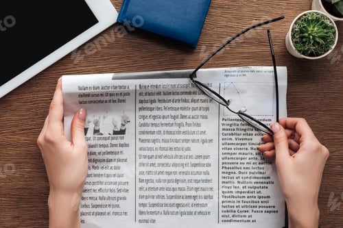 Preview: cropped image of journalist holding newspaper and glasses at wooden table